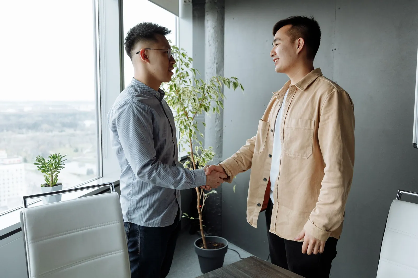 Hai người bắt tay nhau trong văn phòng cạnh cửa kính