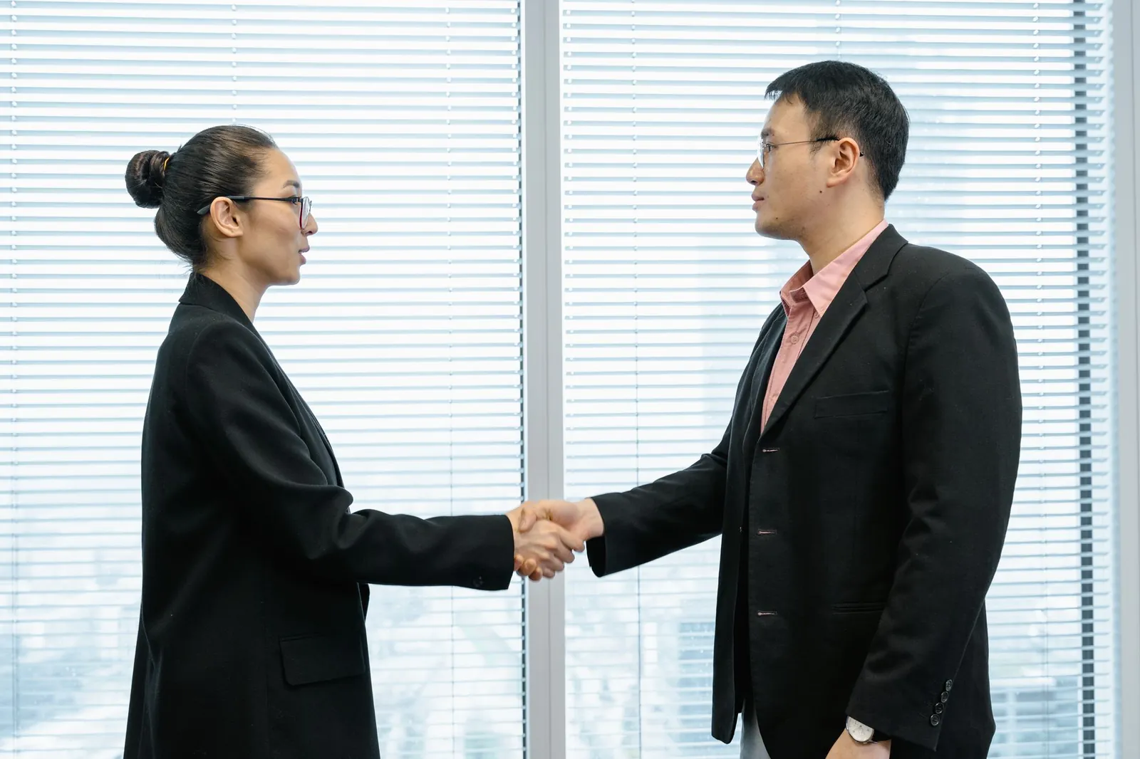 Hai người mặc vest bắt tay nhau trước cửa kính văn phòng