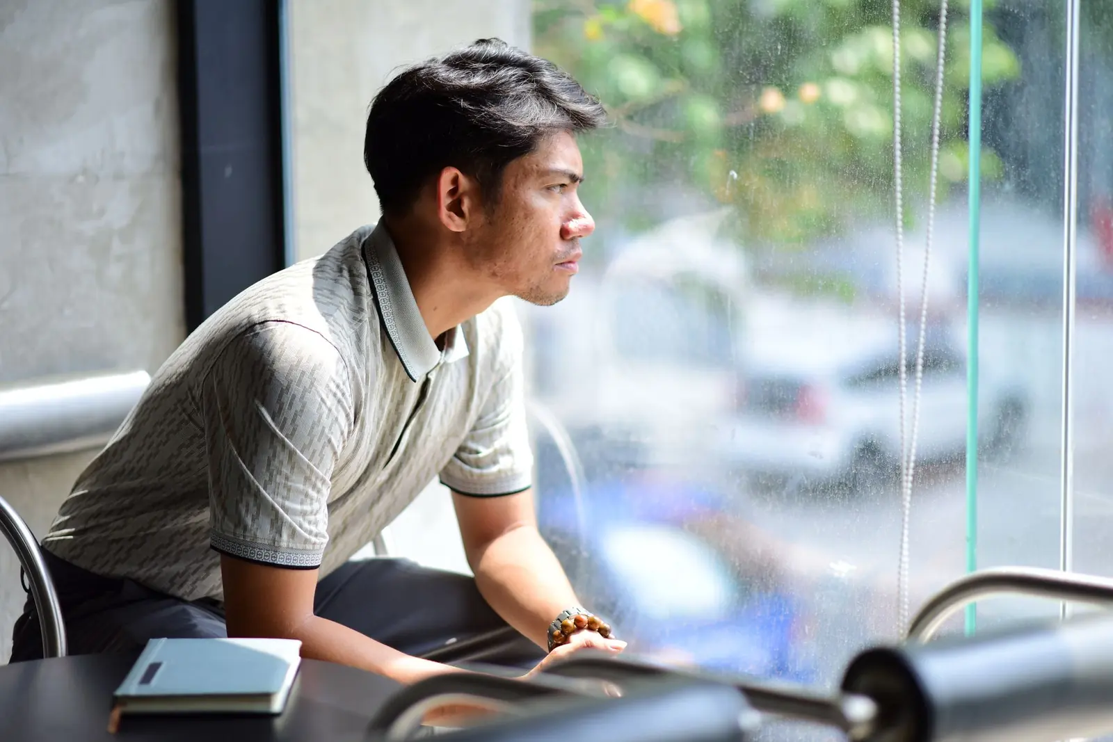 Người đàn ông trẻ ngồi bên cửa kính quán cà phê, nhìn ra ngoài